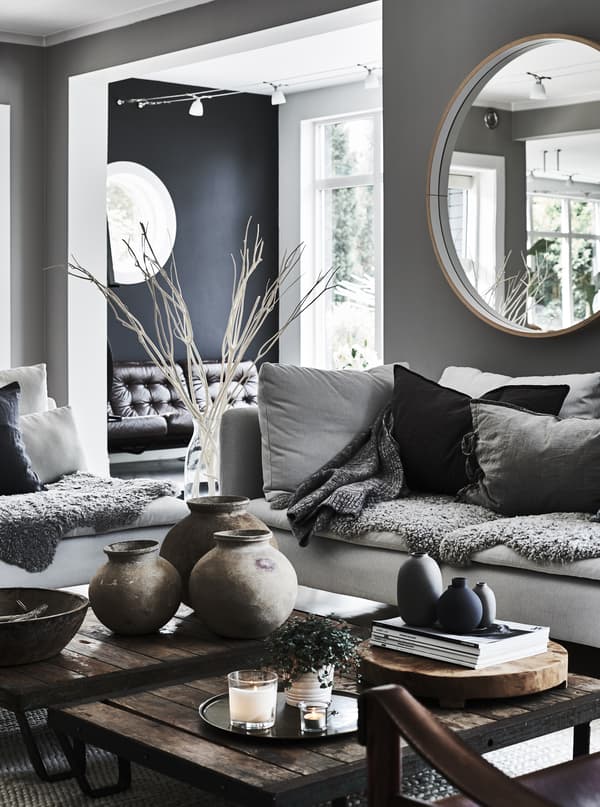 A living room with two grey sofas facing inwards decorated with lots of cosy cushions and coffee tables in brown wood.