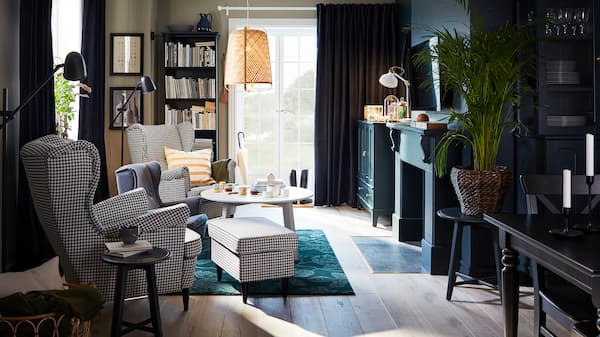 A living room with two houndstooth-patterned wing chairs, a green rug, a pendant lamp in bamboo and a round coffee table.