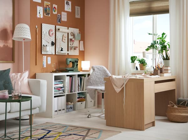 A living room with white furniture and soft pink accents has a creativity corner with a sewing machine and oak desk.