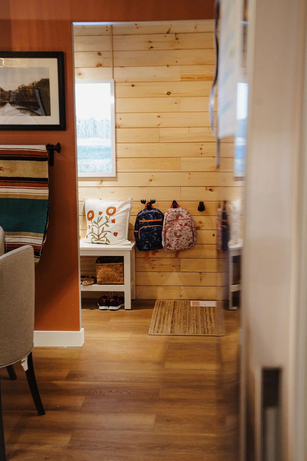 A long shot of a room setting showing the back of a wall and wooden slats with hooks and hanging childrens backpacks.