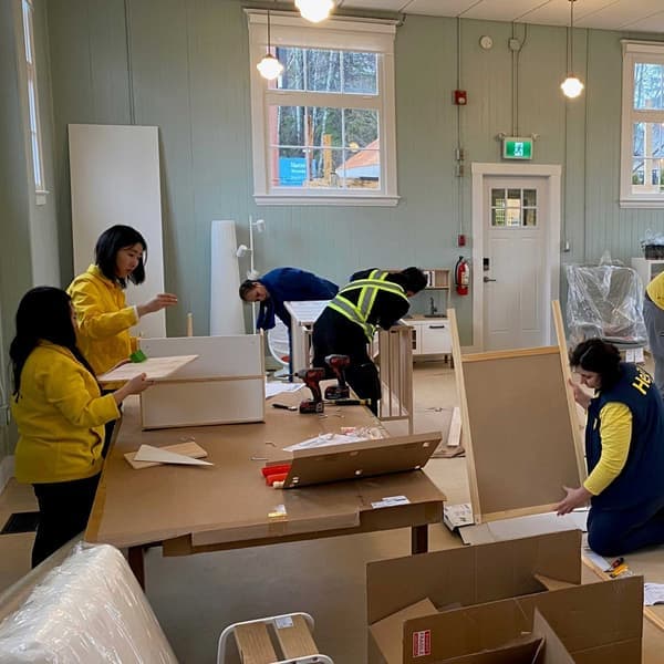 A long shot of different coworkers working to assemble furniture.