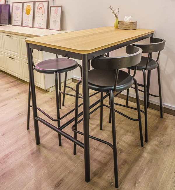 A long wooden table with four black high-chairs tucked in the table.