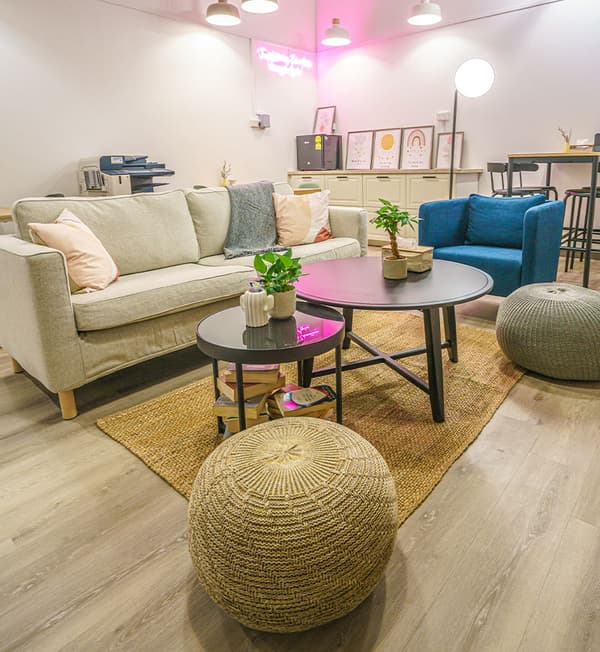 A lounge area featuring a cream sofa, blue sofa chair and coffee tables placed on top a rug.