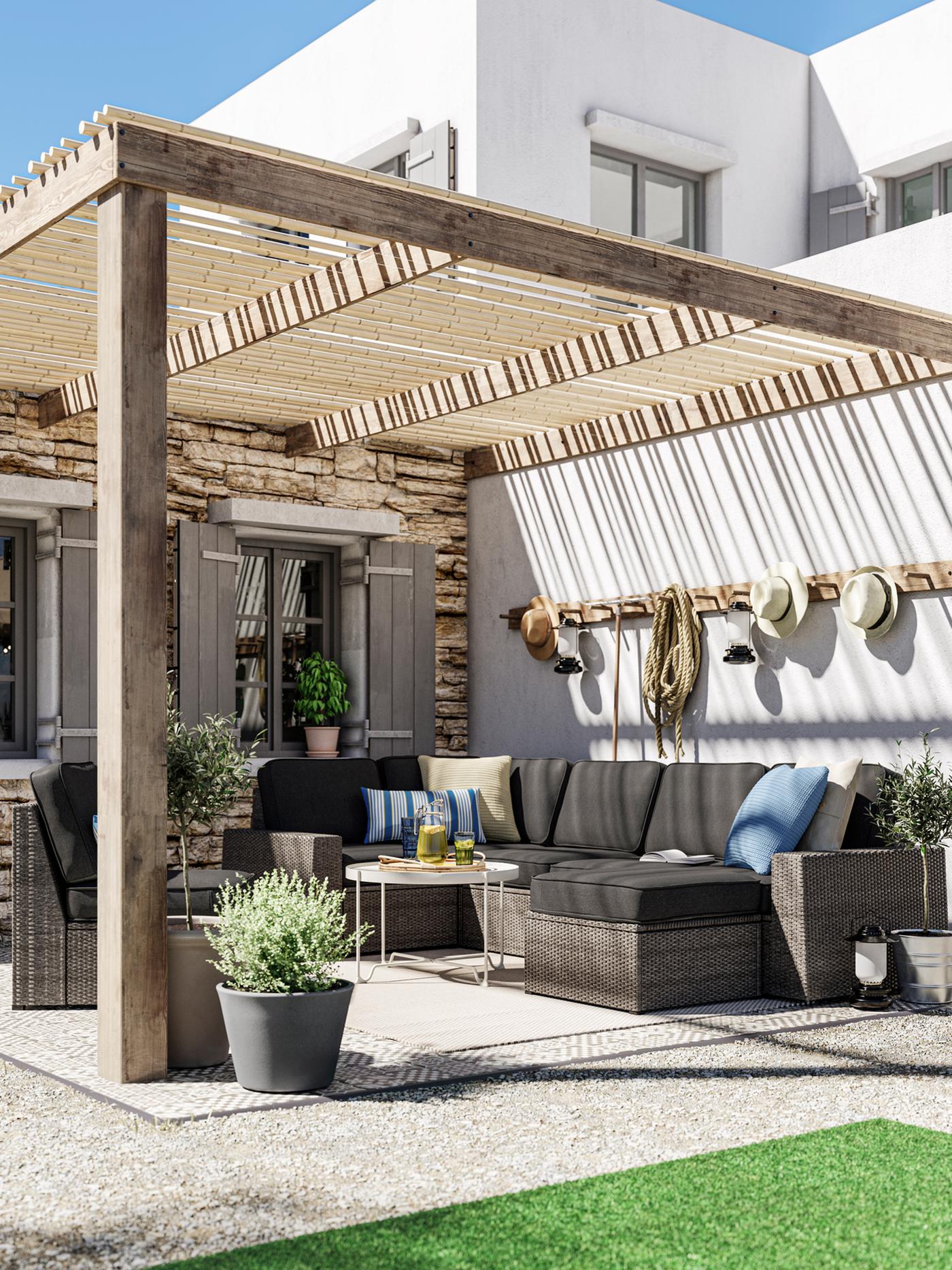 A lounge area with a dark grey outdoor sofa with anthracite cushions, a beige coffee table, decking and potted plants.