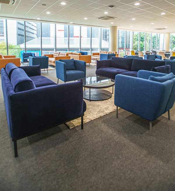 A lounge area with blue and mustard yellow sofas placed on a grey carpeted floor.