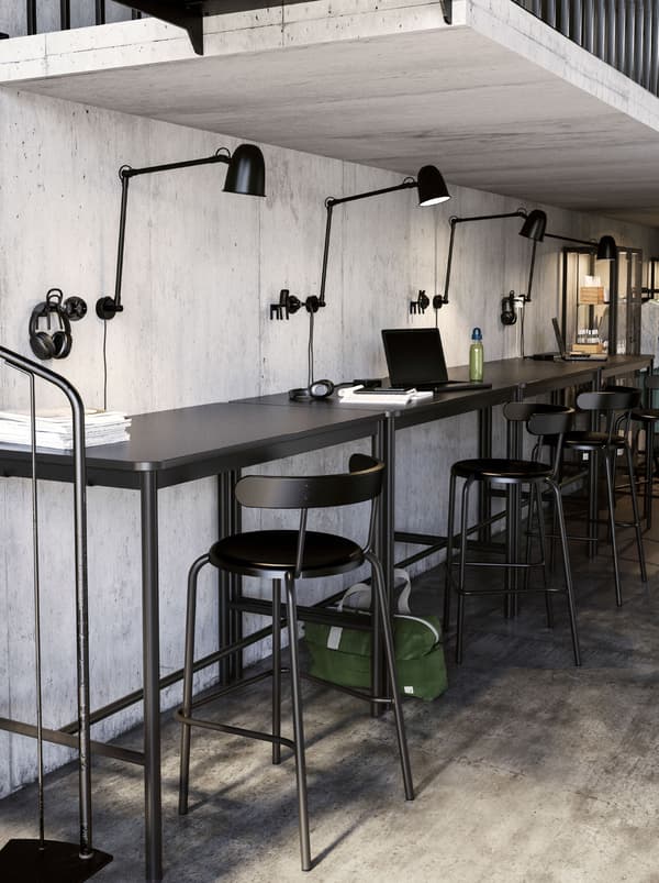 A low-ceilinged co-working space with workstations along a bar, each with a SKURUP work/wall lamp and YNGVAR bar stool.