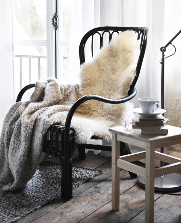 A LUDDE sheepskin and soft grey throw on a black wicker IKEA armchair in a rustic bedroom.