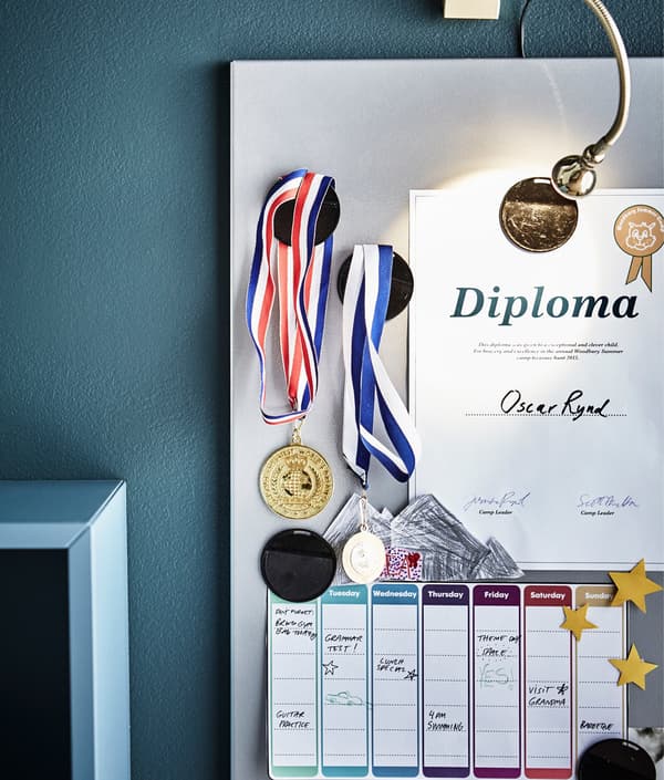 A magnetic board displaying medals, a certificate and a weekly schedule.
