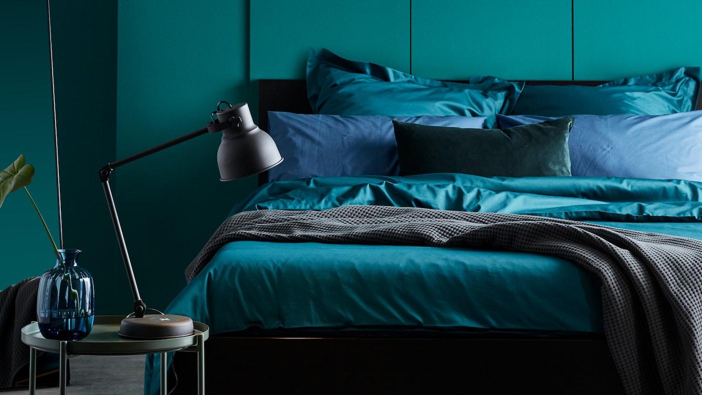 A MALM bed with bedding including dark green LUKTJASMIN bed linen stands against a green wall in a bedroom.