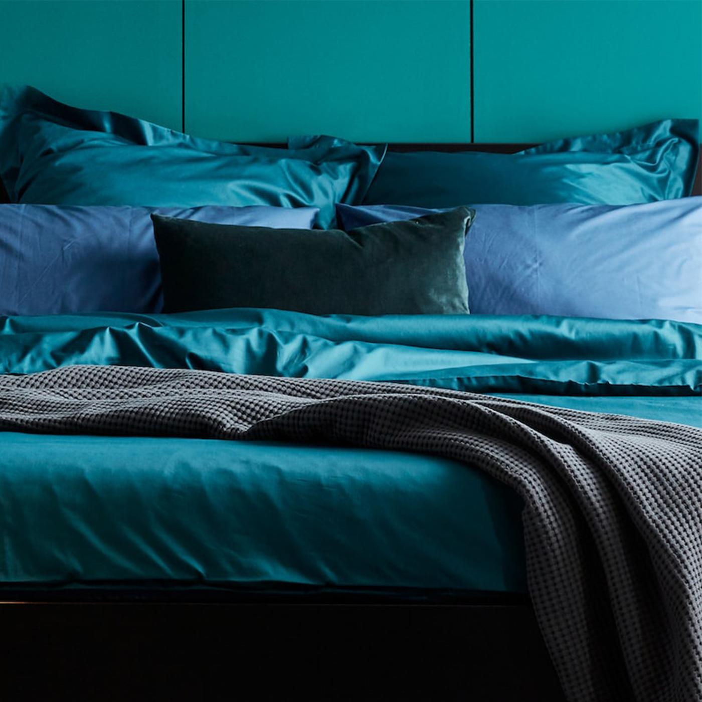 A MALM bed with bedding including dark green LUKTJASMIN bed linen stands against a green wall in a bedroom.