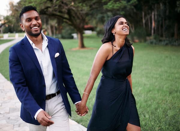 A man and a woman, both wearing formal clothing, are holding hands whilst walking. They are both laughing.