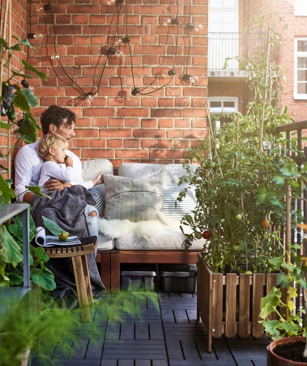 A man and child sitting on a bench next to a red brick wall on a balcony.