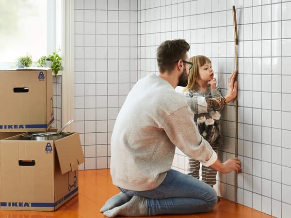 A man and his daughter measuring a wall with a measuring tape.