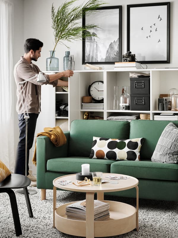 A man getting something out of a cupboard at the end of open shelves behind a PÄRUP sofa and with pictures on the wall above.