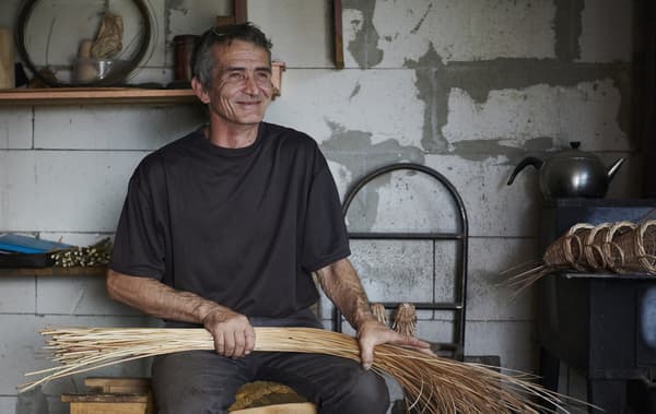 A man holding a bunch of cane in a workshop.