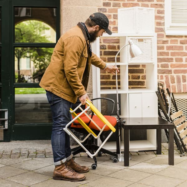 A man holding a small table in one hand and a floor lamp in another.