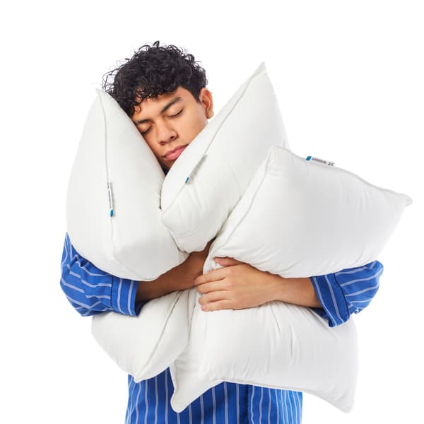 A man hugging 3 pillows while wearing blue striped pajamas on a white background