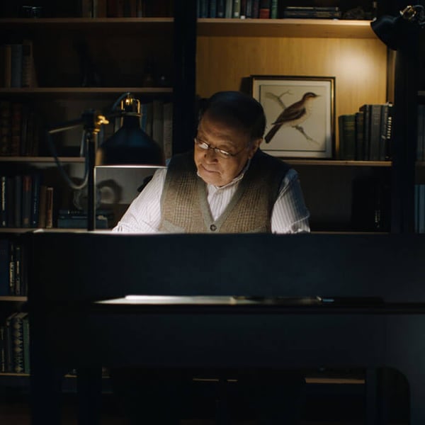 A man in a dark room working from home sitting at his desk with his RANARP work lamp turned on