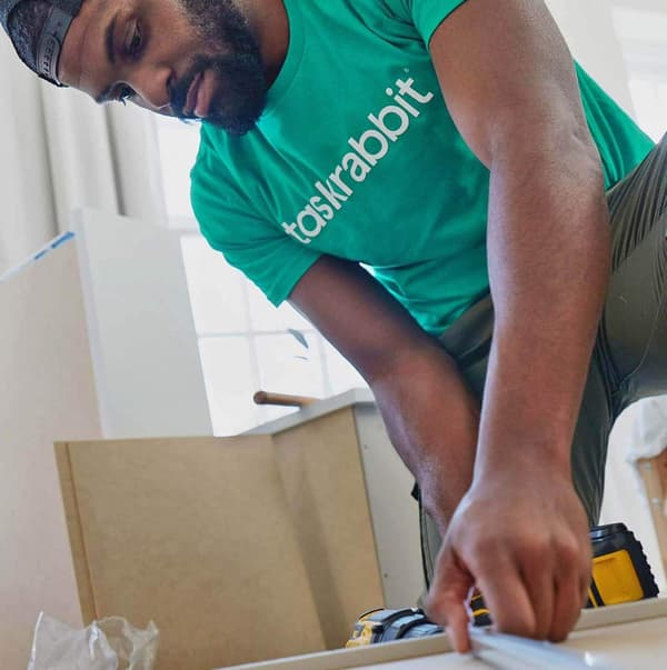 A man in a green taskrabbit shirt putting together furniture.