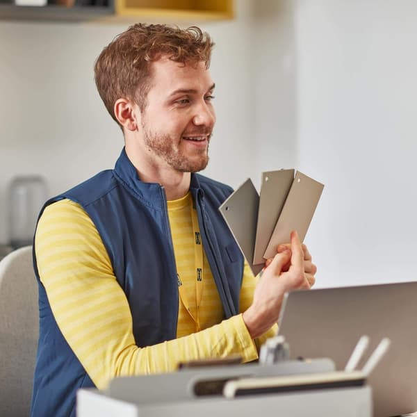 A man in front of a laptop holding 3 color design samples up.