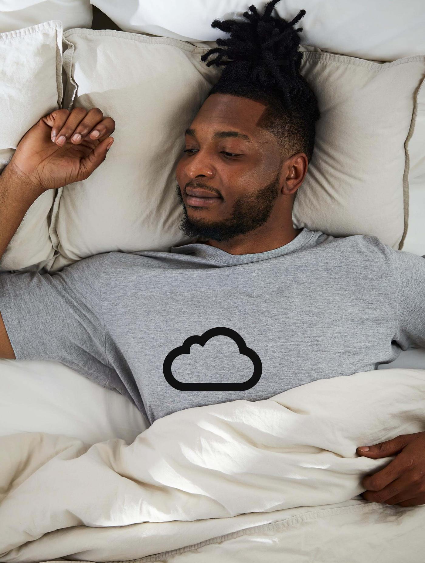 A man in pajamas lying down on a bed with a cloud icon on the image.