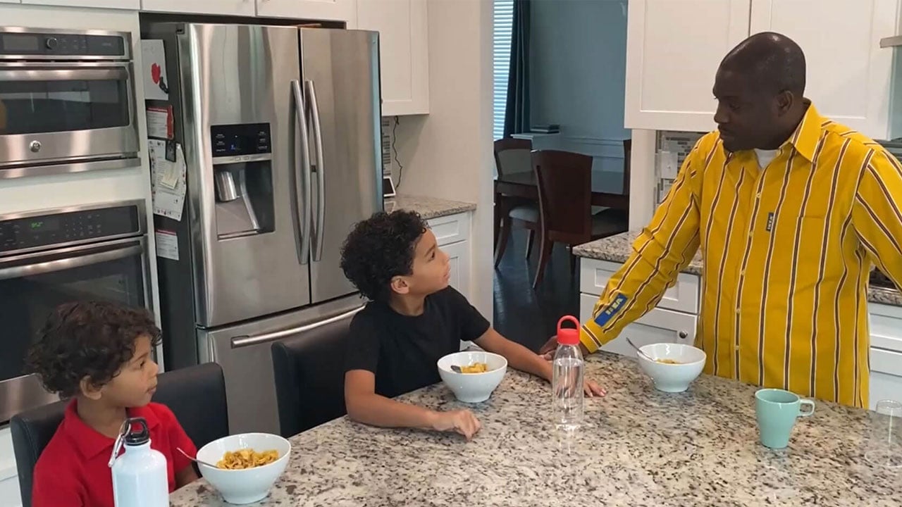 A man in yellow IKEA uniform standing talking to two young children around a kitchen countertop island.