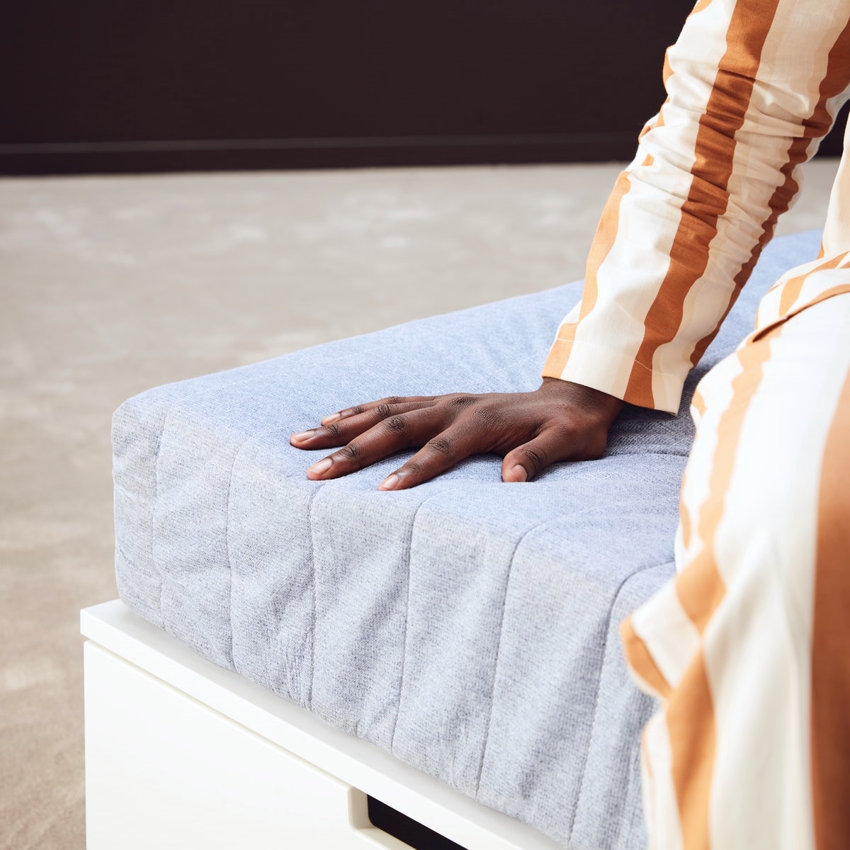 A man is sitting on a mattress and putting his hand on a mattress