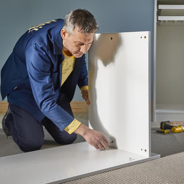 A man is sitting on the floor assembling a kitchen cabinet.