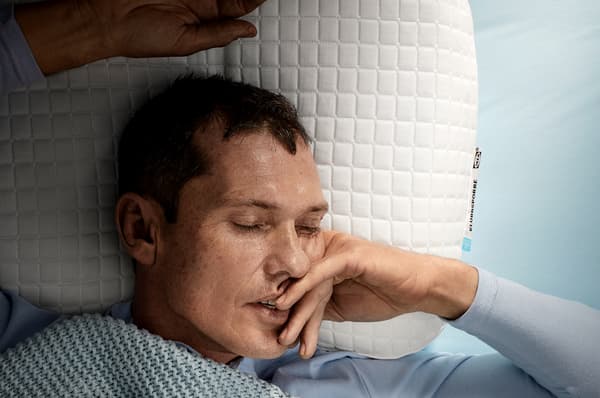 A man, laying on his back, is sleeping deeply on IKEA KLUBBSPORRE ergonomic pillow.