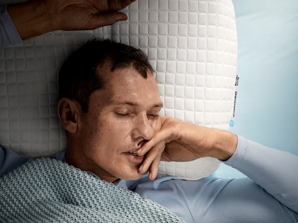 A man, laying on his back, is sleeping deeply on IKEA KLUBBSPORRE ergonomic pillow.