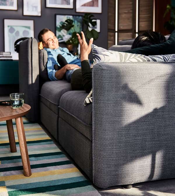 A man relaxing on a grey VALLENTUNA modular sofa.