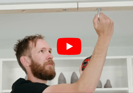 A man screws a board into the ceiling, a red Youtube play button sits overlay.