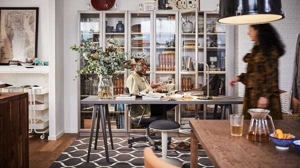 A man sitting at a NÄRSPEL desk in front of three BILLY bookcases filled with books and mementos.