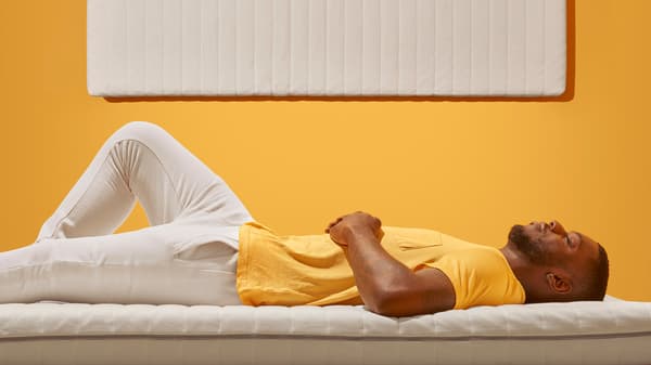 A man sleeping on a mattress with a yellow t-shirt and a white background