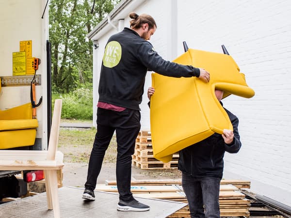 A man standing in the back of a truck passes a yellow STRANDMON armchair down to a person standing behind the truck.
