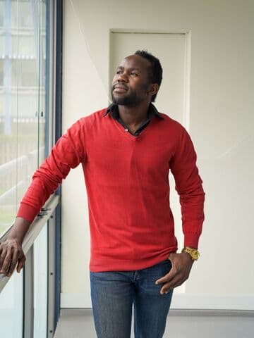 A man standing on a balcony in a red shirt looking out of the window.