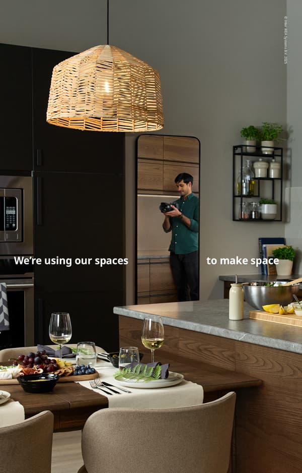 A man takes a photo in a kitchen, reflected in a rectangular mirror on a wall, with wine glasses and a plated meal on the table and the text, “We’re using our spaces to make space.”.