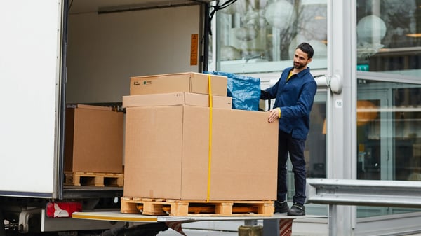 A man unloads a pallet with parcels from a truck loading bay.