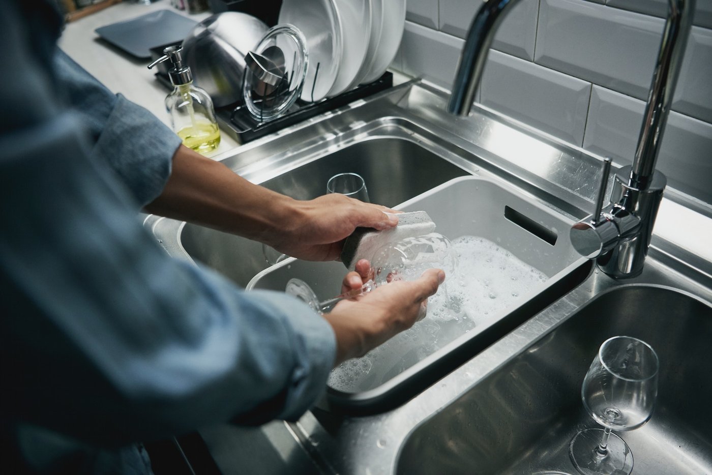 A man washing dishes in the kitchen, using the ÄLMAREN kitchen mixer tap.
