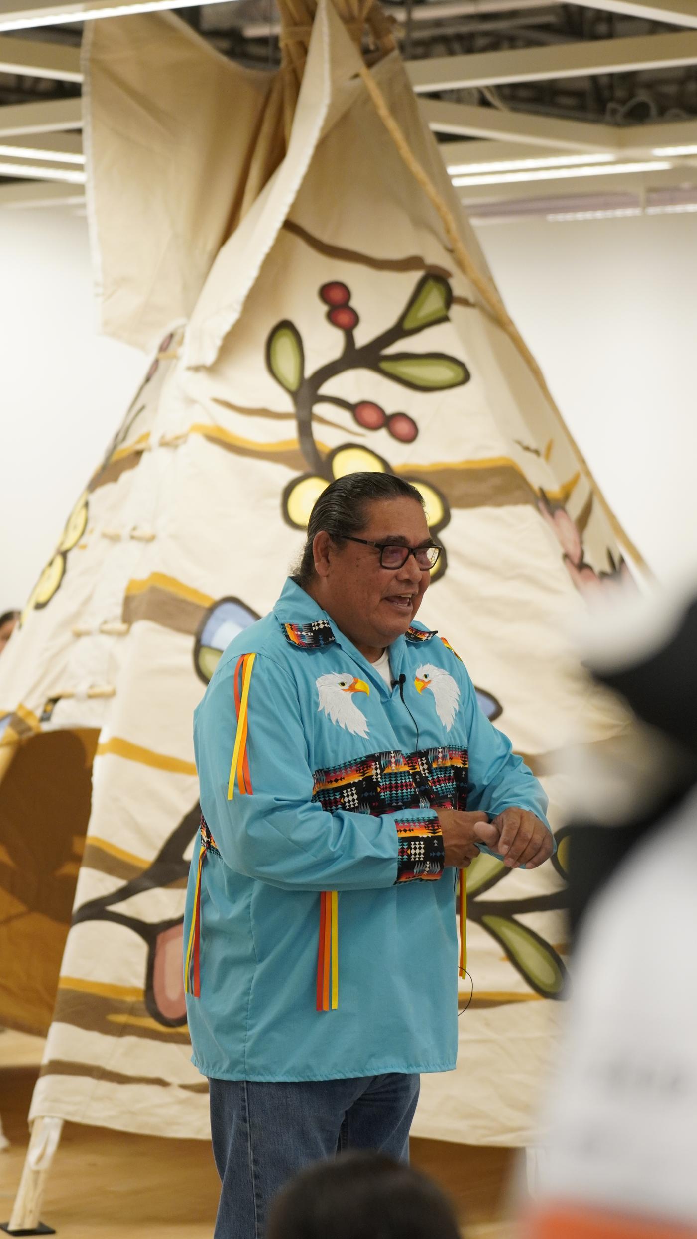 A man wearing a long blue shirt is presenting something to a crowd of people.