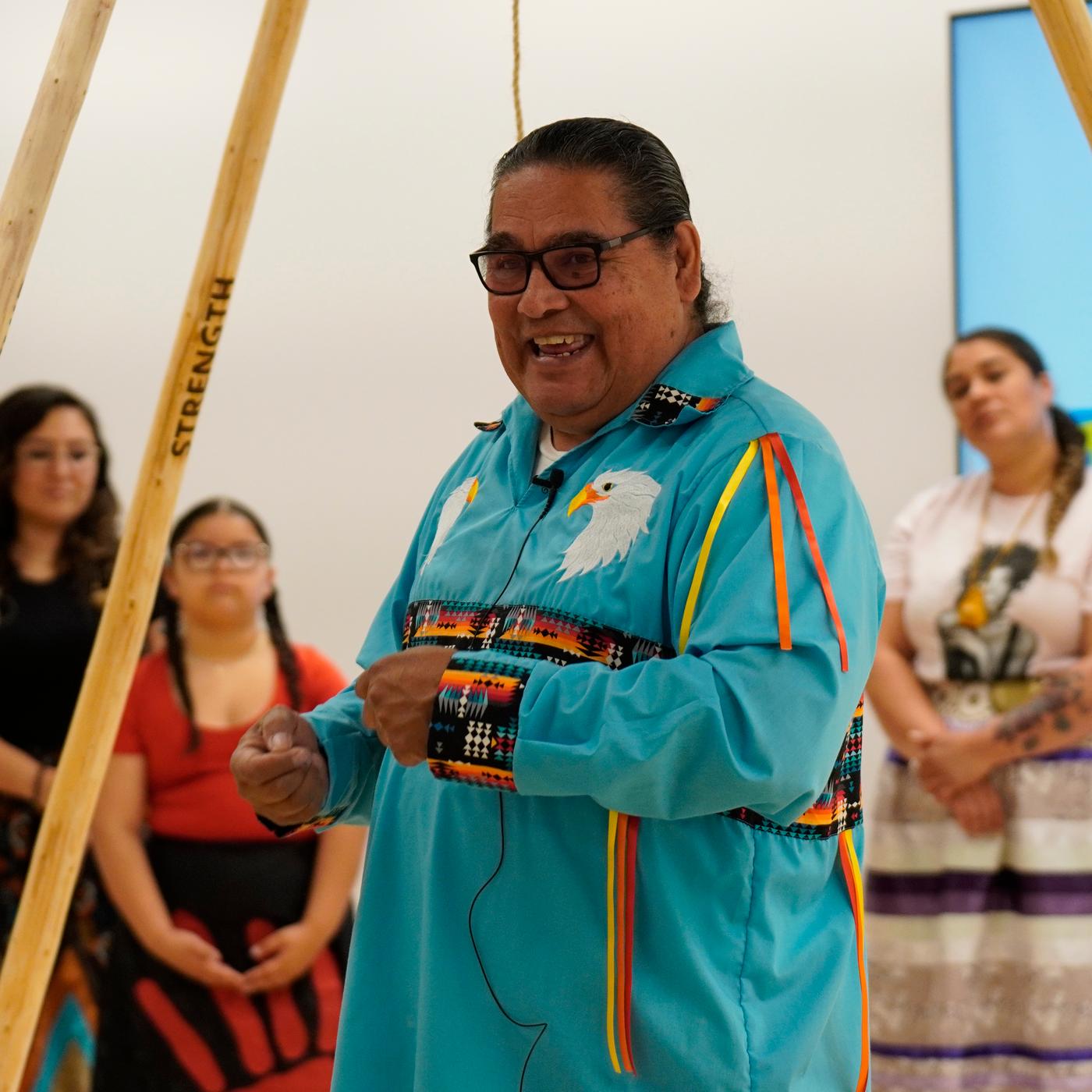A man wearing a long blue shirt is smiling facing a crowd of people.