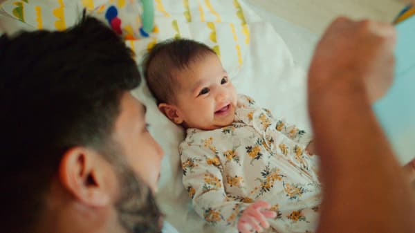A man with a beard entertains a smiling baby on a bed.