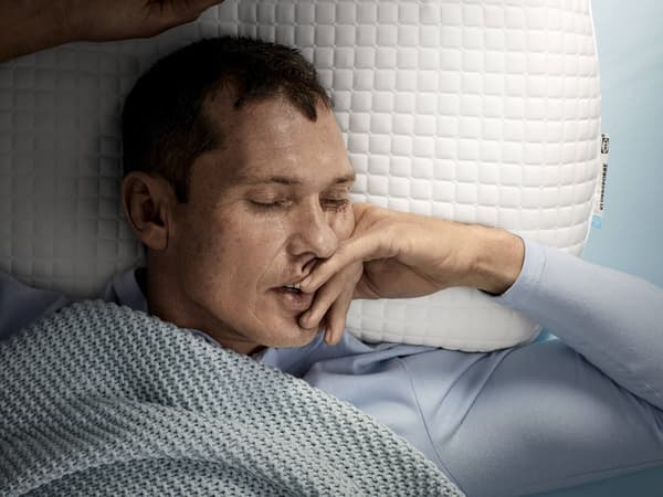 A man with dark hair lying on his back on a white ergonomic pillow.