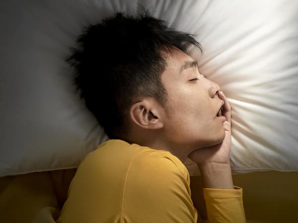 A man with dark hair lying on his side on a white pillow.