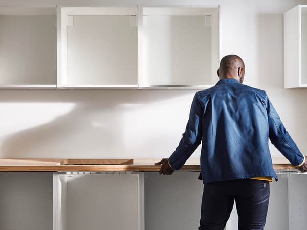 A man with his back turned in a partially finished kitchen and holds kitchen countertop.