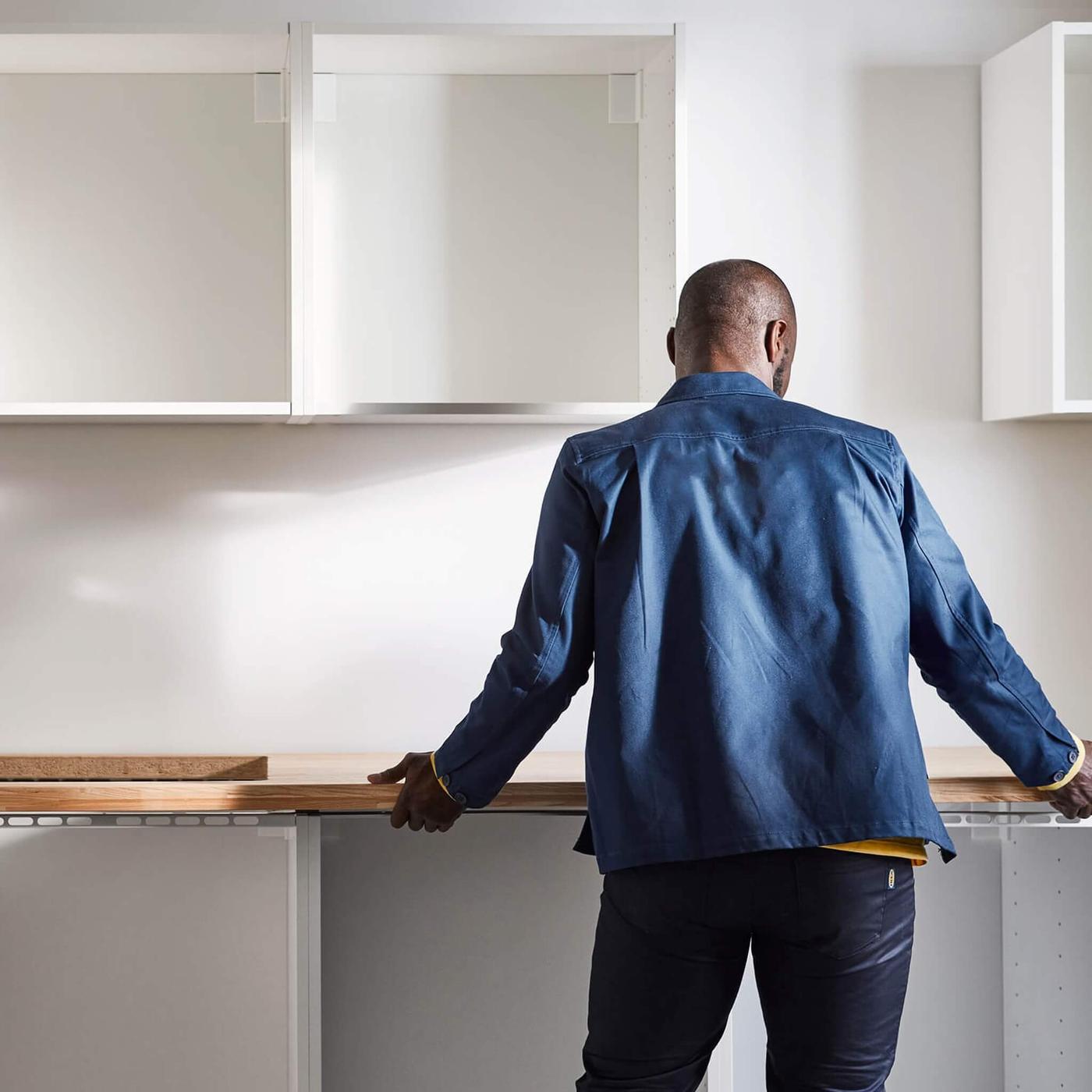 A man with his back turned into a partially finished kitchen and holding a kitchen countertop.
