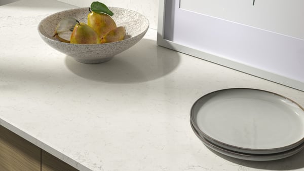 A marble tan countertop with plates and a bowl of fruit on it.