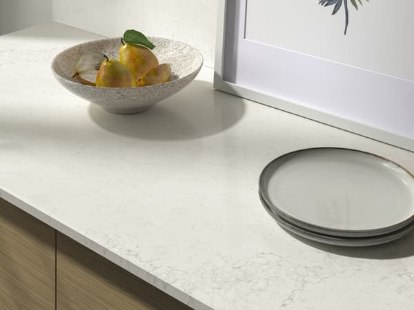 A marble tan countertop with plates and a bowl of fruit on it.