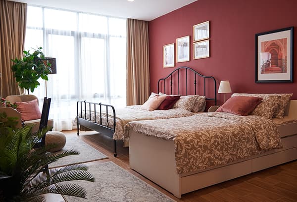A maroon room featuring two beds and decorative plants.