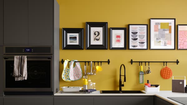 A matt anthracite kitchen with a white marble effect worktop, plus black rails and pictures in black frames on a yellow wall.